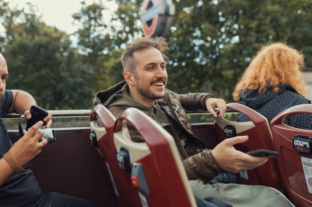 Happy traveler enjoying an open-top bus tour in London with friends.